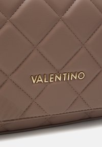 Hnedá prešívaná taška z faux kože so zlatým logom "Valentino". Povrch má hladkú textúru a prešívaný diamantový vzor.