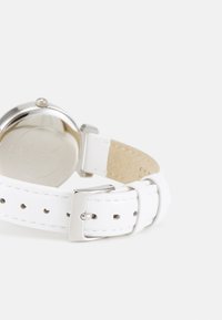 Bracelet de montre en cuir blanc avec boucle en métal argenté, boîtier en acier inoxydable rond et dos gravé. Texture lisse ; design épuré.