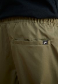 Olíva zöld rövidnadrág texturált anyagból, rugalmas derékkal és egy kis hátsó zsebbel, amelyen fekete Nike logó címke található.