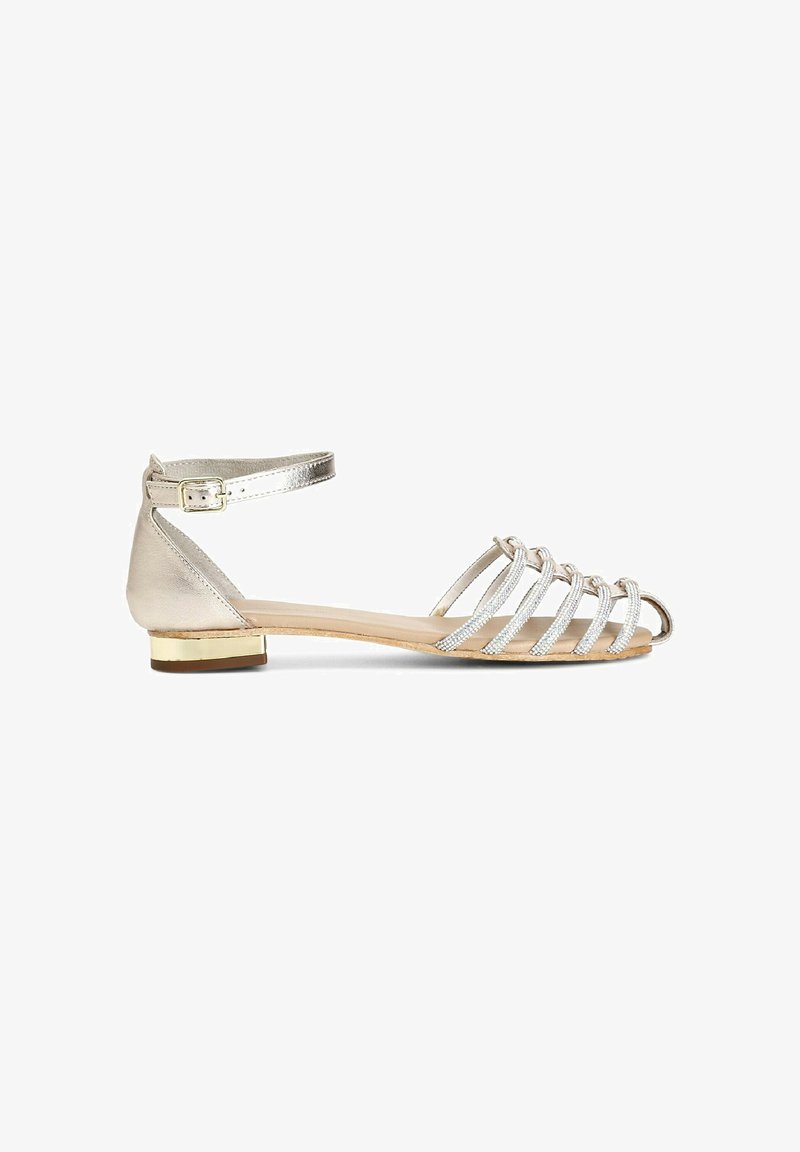 Silverfärgad metallic sandal med korsade remmar, öppen tå och vristrem. Platt klack med guldaccent. Slät textur och minimalistisk design.