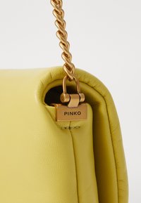 Borsa a tracolla in pelle gialla con finitura testurizzata, dotata di una tracolla in catena dorata e di un chiusura in metallo dorato con marchio.