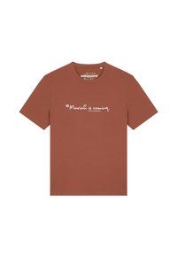 T-shirt couleur rouille en coton, avec des manches courtes et un col rond. Un texte imprimé en blanc indique "Mariah arrive."