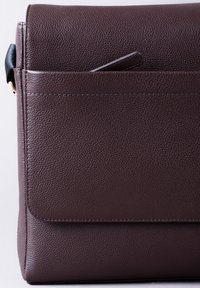 Brown, textured leather messenger bag with a flap, outer pocket, and subtle stitching detail. Compact design suitable for daily use.