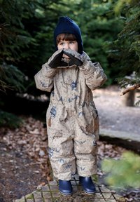 Beige waterdicht skipak met blauwe patronen van dieren en bergen, geïsoleerde voering, elastische taille en diepblauwe rubberen laarzen.