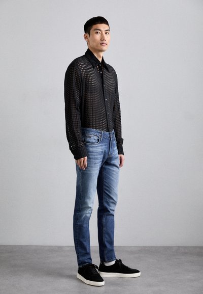 Black checkered button-up shirt with long sleeves, paired with light blue denim jeans and black sneakers. Smooth and textured fabric details.