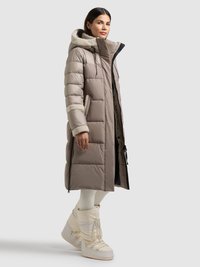 Abrigo largo acolchado en color topo con capucha forrada de piel sintética, que cuenta con bolsillos laterales y cierre delantero con cremallera, combinado con botas blancas aislantes.