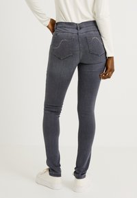 Jeans skinny de color gris oscuro con una cintura alta, bolsillos traseros con costuras sutiles y una textura de denim suave. Combinados con zapatillas blancas.