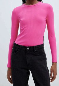 Haut ajusté à manches longues côtelées de couleur rose vif, associé à un jean en denim noir taille haute. Présente un col rond et une texture lisse.