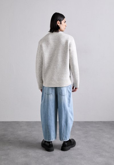 Γκρι πλεκτό πουλόβερ με ριχτές μανσέτες και στρίφωμα, σε συνδυασμό με χαλαρές ανοιχτό μπλε τζιν παντελόνες και μαύρες πλατφόρμες.