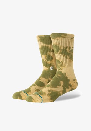 Chaussettes montantes tie-dye vertes et beiges avec texture côtelée, arborant un patch logo et des accents turquoise sur la zone des orteils.
