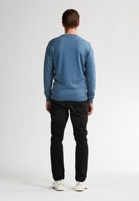 Pulover albastru cu mâneci lungi și manșete strâmte, purtat cu pantaloni negri și adidași albi. Țesătura pare netedă și ușoară.