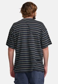 Oversized striped t-shirt in dark blue, featuring horizontal stripes in cream and beige. Round neckline and short sleeves. Cotton material.