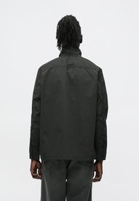 Black jacket with a high collar, made of lightweight material. Features a slightly wrinkled texture and a relaxed fit.
