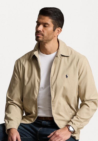 Μπεζ ελαφρύ μπουφάν με λεία υφή, μπροστινό φερμουάρ και αιχμηρό γιακά. Διαθέτει διακριτικό λογότυπο στο αριστερό στήθος και πλαϊνές τσέπες.