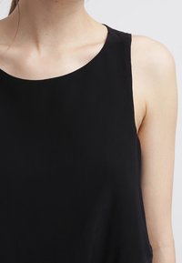 Top nero senza maniche con scollatura rotonda, realizzato in un tessuto leggero. Caratterizzato da una texture liscia e da un design semplice e minimalista.