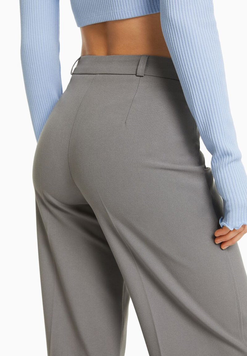 Pantalons gris ajustés avec une texture lisse et une coupe à jambe large. Dotés d'une taille mi-haute et de poches latérales discrètes. Pull bleu côtelé court.