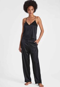 Camisole en satin noir avec des bretelles fines et un décolleté en V, associée à un pantalon large en satin assorti, présentant une texture lisse et une coupe décontractée.