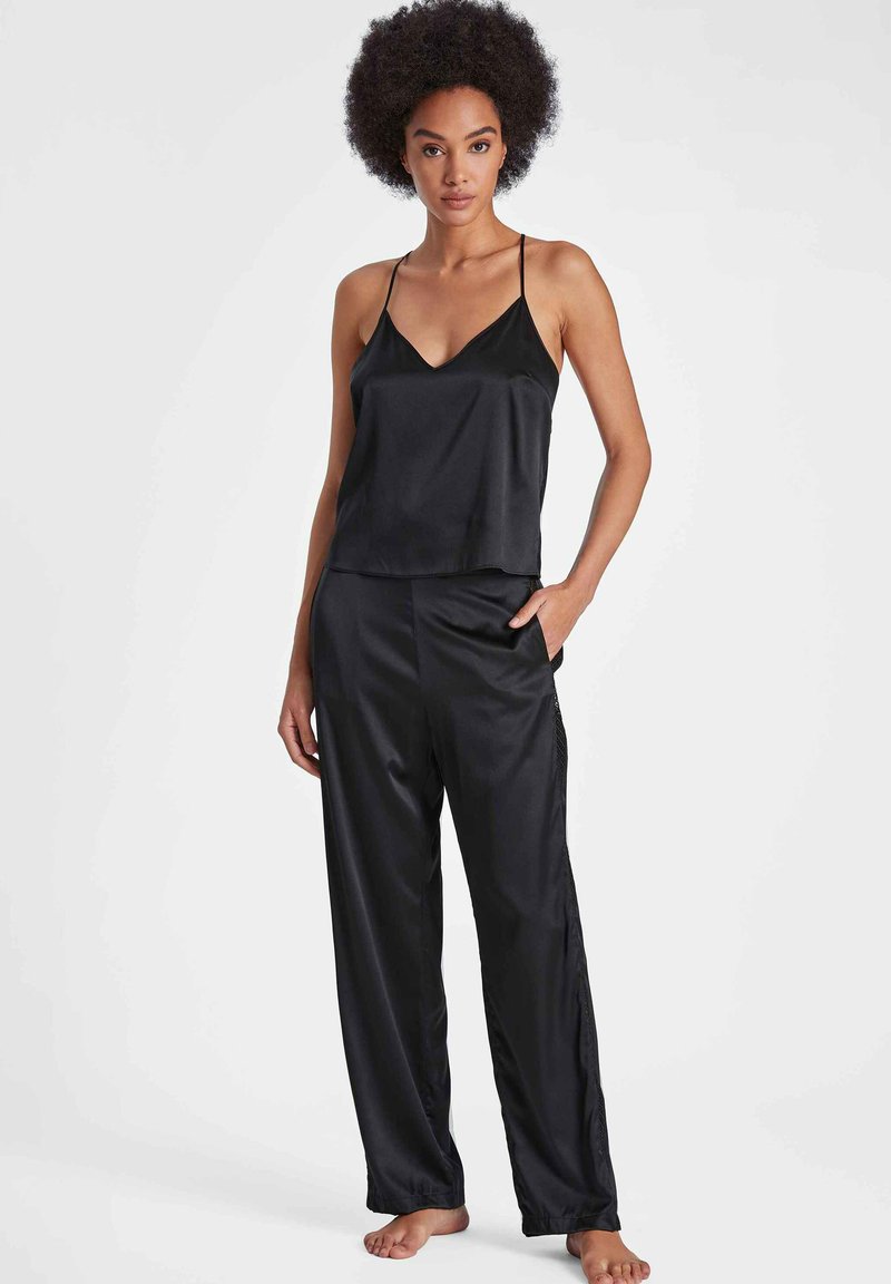 Camisole en satin noir avec des bretelles fines et un décolleté en V, associée à un pantalon large en satin assorti, présentant une texture lisse et une coupe décontractée.