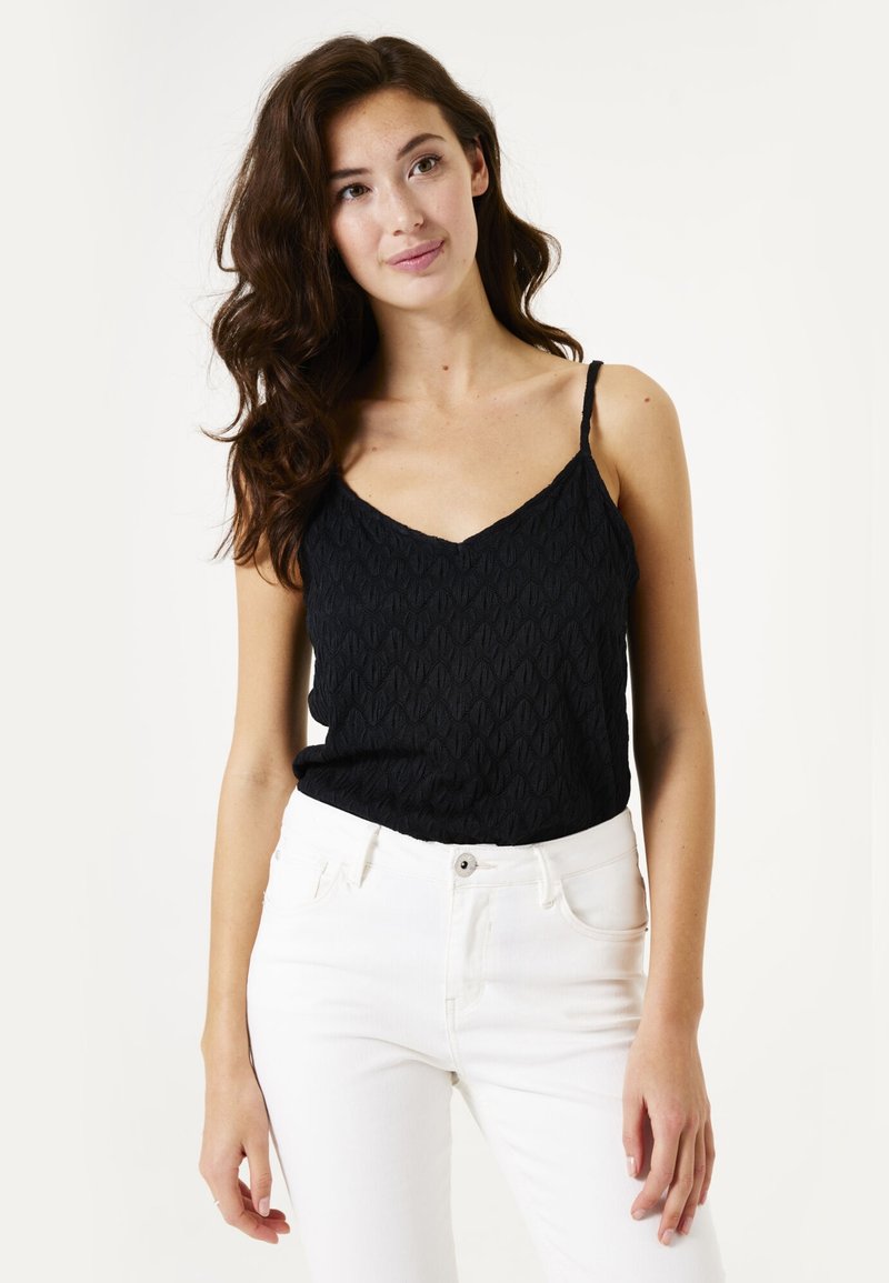 Top en camisole noir à motifs avec des bretelles fines, présentant un décolleté en V, associé à un jean blanc moulant. Texture de tissu lisse.