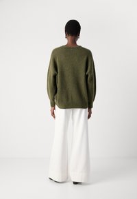 Grön oversized tröja med en texturerad yta, med rundad halsringning och en knappdetalj på baksidan. Kombinerad med vita byxor med vida ben.