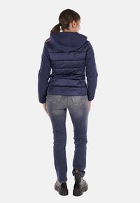 Giacca puffer blu navy con cappuccio, texture a coste e silhouette aderente, abbinata a jeans blu e stivali neri con lacci.