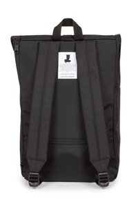Svart ryggsäck med rektangulär form, vadderade remmar, ett handtag på toppen och en etikett med en stiliserad bild och text på baksidan.
