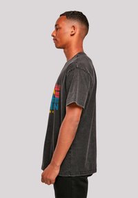 Black graphic t-shirt with short sleeves, boxy shape, and multicolored text design. Features a faded texture and visible stitching details.