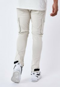 Pantalones cargo color beige claro con bolsillos laterales, de corte ajustado y puños acanalados. Llevados con zapatillas Nike blancas con acentos negros.
