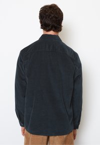 Ciemnoniebieska koszula ze sztruksu z ostrym kołnierzem i pionową fakturą prążków, z długimi rękawami i zaokrąglonym dołem.