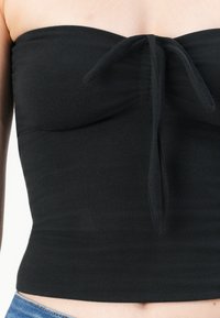 Top negro sin tirantes con un diseño ajustado, tela texturizada y un detalle de lazo en la parte delantera. Se sitúa por encima de la cintura, acomodando diversas tallas.