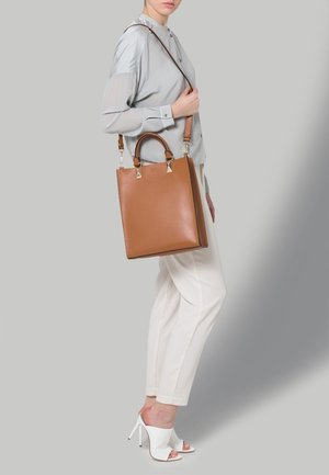 Hnědá kožená tote taška s dvojitými horními uchy a odnímatelným popruhem, se strukturovaným tvarem a zlatými kovovými doplňky.
