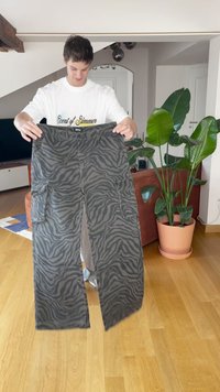 Fekete és szürke zebra csíkos mintázatú cargo nadrág, amely két nagy oldalzsebet és bő szabást kínál. Az anyag texturált felületű.