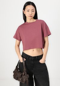 Top curto, de manga curta, em algodão mauve. Combinado com calças de ganga pretas de cintura alta e uma bolsa de couro castanho-escuro com vários bolsos.