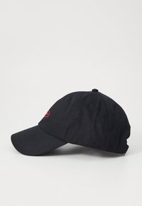 Svart baseballcap laget av bomull, med buet skygge, seks paneler, og en rød logo brodert på fronten. Justerbart belte bak.
