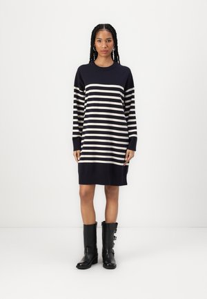 Robe pull rayée bleu marine et crème avec des manches longues, des poignets côtelés et une coupe décontractée, portée avec des bottes noires jusqu'aux genoux.