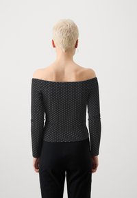 Juodas off-shoulder viršus ilgomis rankovėmis, su baltais taškeliais ir prigludusia forma. Sklandus audinys su lengvu blizgesiu.