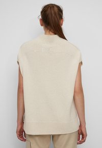 Haut sans manches beige en tricot avec un col et un ourlet côtelés. Texture lisse, légèrement ajusté. Le dos présente un détail côtelé horizontal.