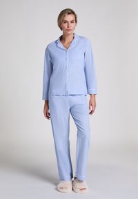 Ljusblå randiga pyjamaser med skjorta med knappar och långa byxor, som har en bröstficka och kontrasterande kant. Mjuk tyg; bärs med fluffiga tofflor.