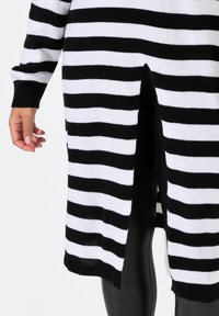 Cardigan a righe bianche e nere in maglia con maniche lunghe, dotato di spacchi laterali all'orlo e un tessuto testurizzato.