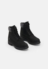 Botines de ante negro con collar acolchado, seis ojales y suela de goma con tacos que presenta un logo en el lateral.