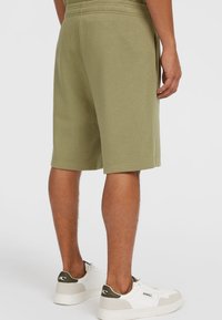Licht olijfgroene katoenen shorts met een elastische tailleband, zijzakken en zichtbare stikdetails, gecombineerd met witte schoenen.