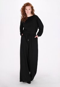 Maglione nero con scollo ampio, maniche lunghe e vestibilità comoda. Abbinato a pantaloni neri larghi con cintura elastica e tasche.