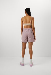 Lyse lilla, teksturerede shorts med elasticitet i taljen og sidesømmer. Et lille logo patch er synligt på den højre bagside.