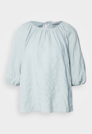 Light blue blouse with a textured plaid pattern, rounded neckline, and gathered sleeves. Features a tie detail at the back.