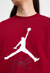 Czerwona bawełniana koszulka z białym konturem skaczącej postaci oraz napisem "Flight" w szarym kolorze poniżej. Okrągły dekolt, krótkie rękawy.