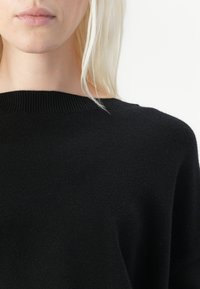 Schwarzer Strickpullover mit geripptem Ausschnitt, weichem Griff und lässiger Passform, cropped Länge und ohne sichtbare Muster oder Hardware-Details.