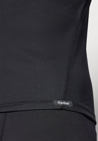 Schwarzes Radtrikot aus leichtem Stoff mit strukturiertem Muster, mit einem GripGrab-Label am Saum und eleganten Nähdetails.
