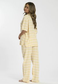 Set di pigiama giallo e bianco a quadretti realizzato in morbido cotone, caratterizzato da una maglietta ampia con maniche corte e pantaloni abbinati con una vestibilità rilassata.