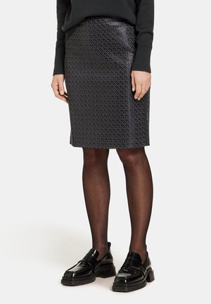 Falda lápiz negra con un sutil patrón geométrico, confeccionada con un material suave. Combinada con unos mocasines negros brillantes y medias opacas.