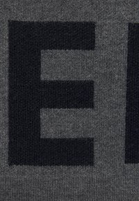 Nahaufnahme eines Textils mit einem grauen Stoff, der ein auffälliges schwarzes Muster aus Buchstaben zeigt. Die Textur wirkt weich und gewebt, mit einer glatten Oberfläche.